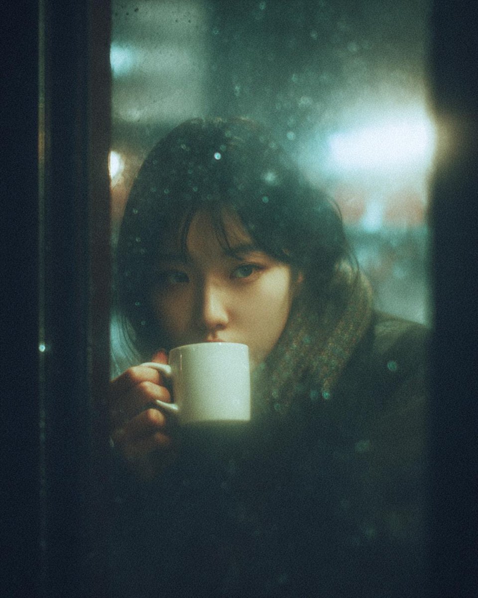 A cinematic, moody photograph of a young woman sitting inside...